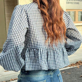 Person wearing a black and white checkered blouse with ruffled details, standing outdoors.